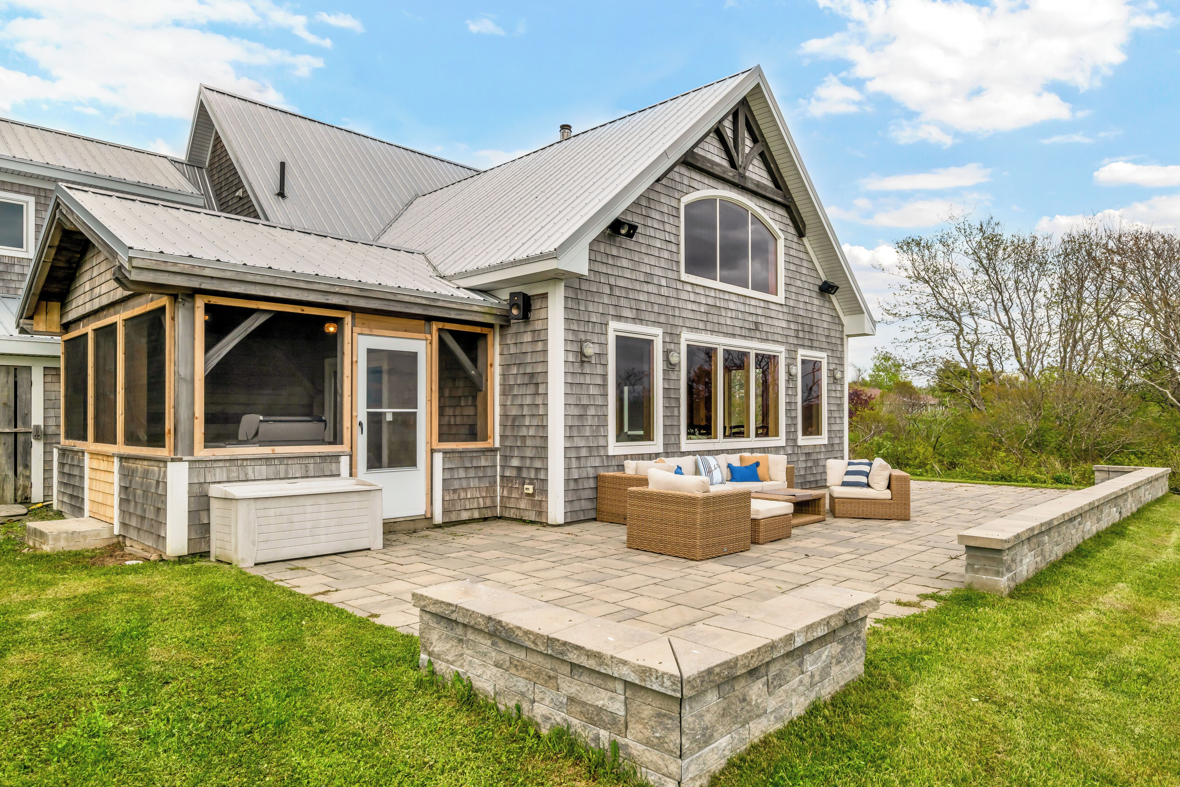 A two-story house with a covered patio, large windows, and a stone retaining wall.