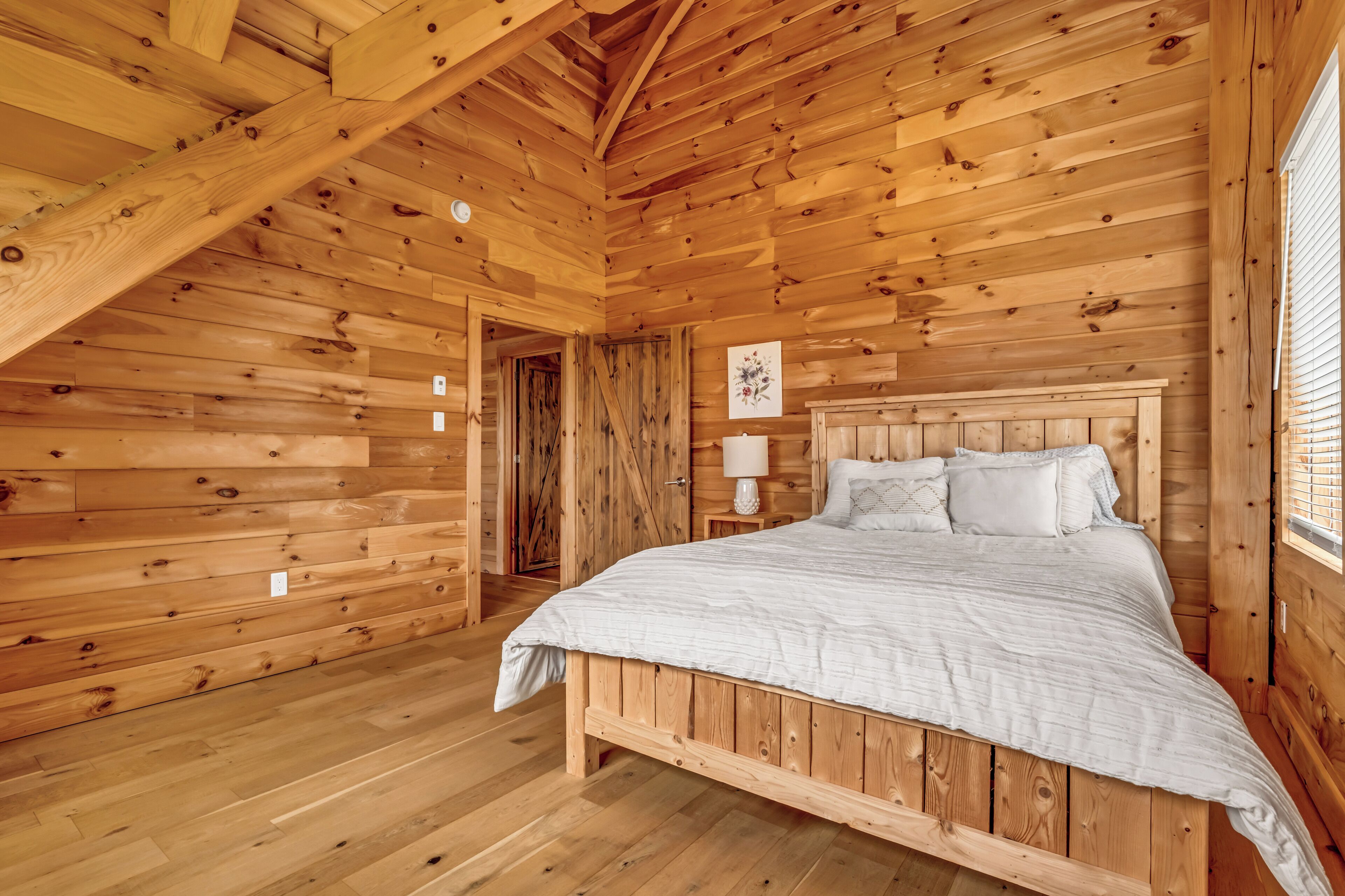 A wooden cabin bedroom with a bed, a nightstand, and a wall-mounted lamp.