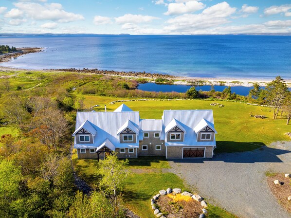 A large, modern house with a metal roof, surrounded by a well-maintained lawn and a view of the ocean. - Beach Front Estate Custom Timber Frame Home on Cleveland Beach 72 (Hubbards)