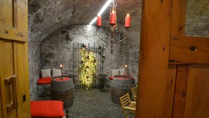 Un interior rústico con paredes de piedra, barriles de madera y una zona de estar acogedora con cojines.