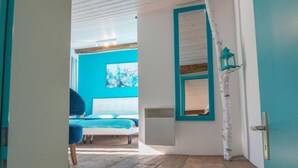 Una escalera conduce a un dormitorio con una pared azul y un ventanal de marco verde azulado.