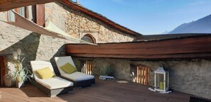 A wooden deck with two lounge chairs, a stone wall, and a lantern. - Chez Constance (Saillon)