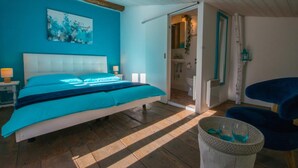 Un dormitorio con una cama grande, una mesita de noche con lámpara, una obra de arte en la pared y vistas al baño.