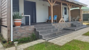 A covered outdoor seating area with stone steps leading up to a patio, two blue chairs, and a wooden pergola. - MALAKA F1 of charm ........ (LE MOULE)