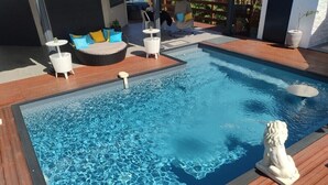 A swimming pool with a wooden deck, a white statue, and a seating area with cushions and a small table. - MALAKA F1 of charm ........ (LE MOULE)