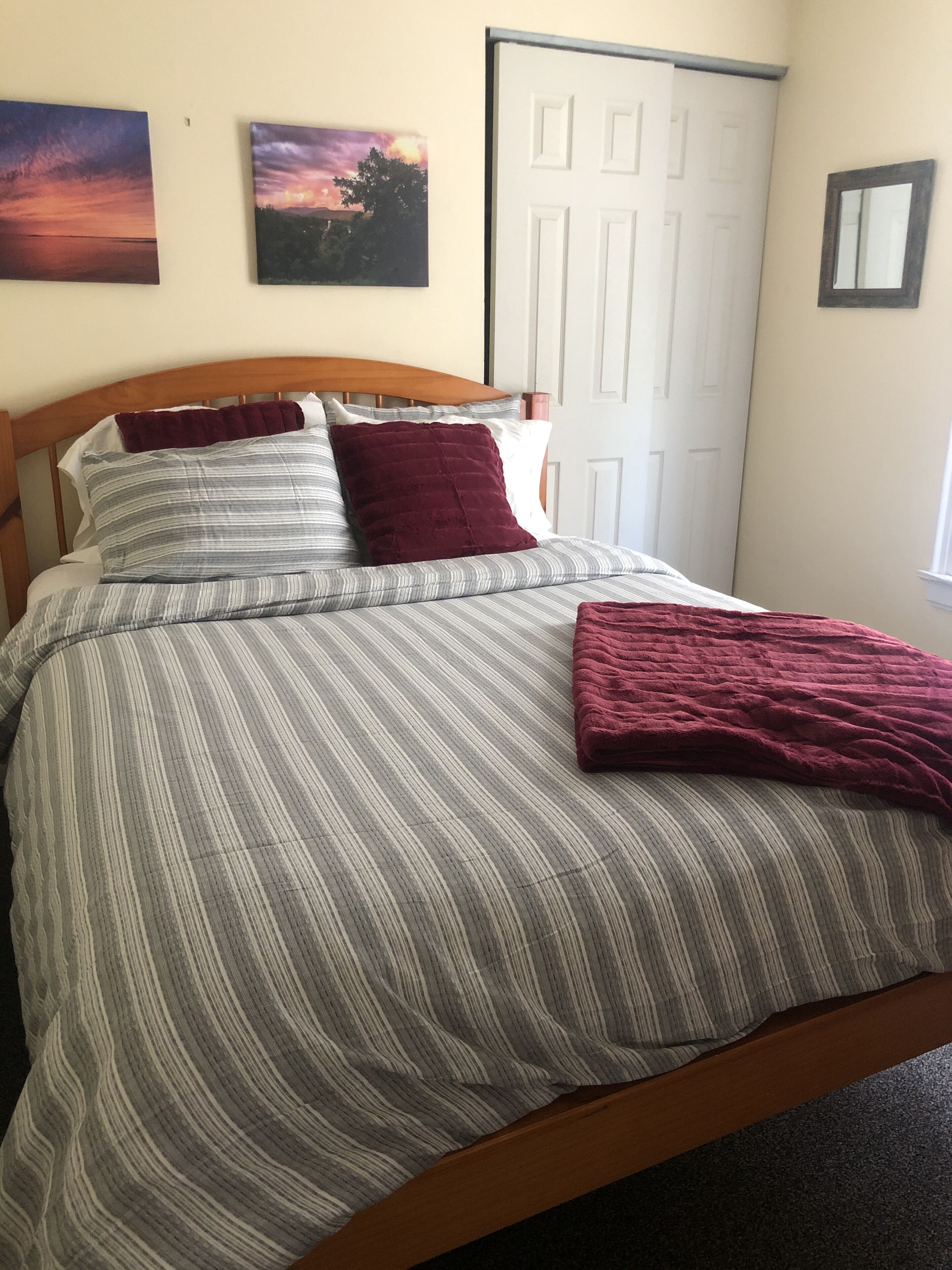 Una cama bien hecha con ropa de cama a rayas y un edredón doblado, un cabecero de madera y dos cuadros colgados en la pared.