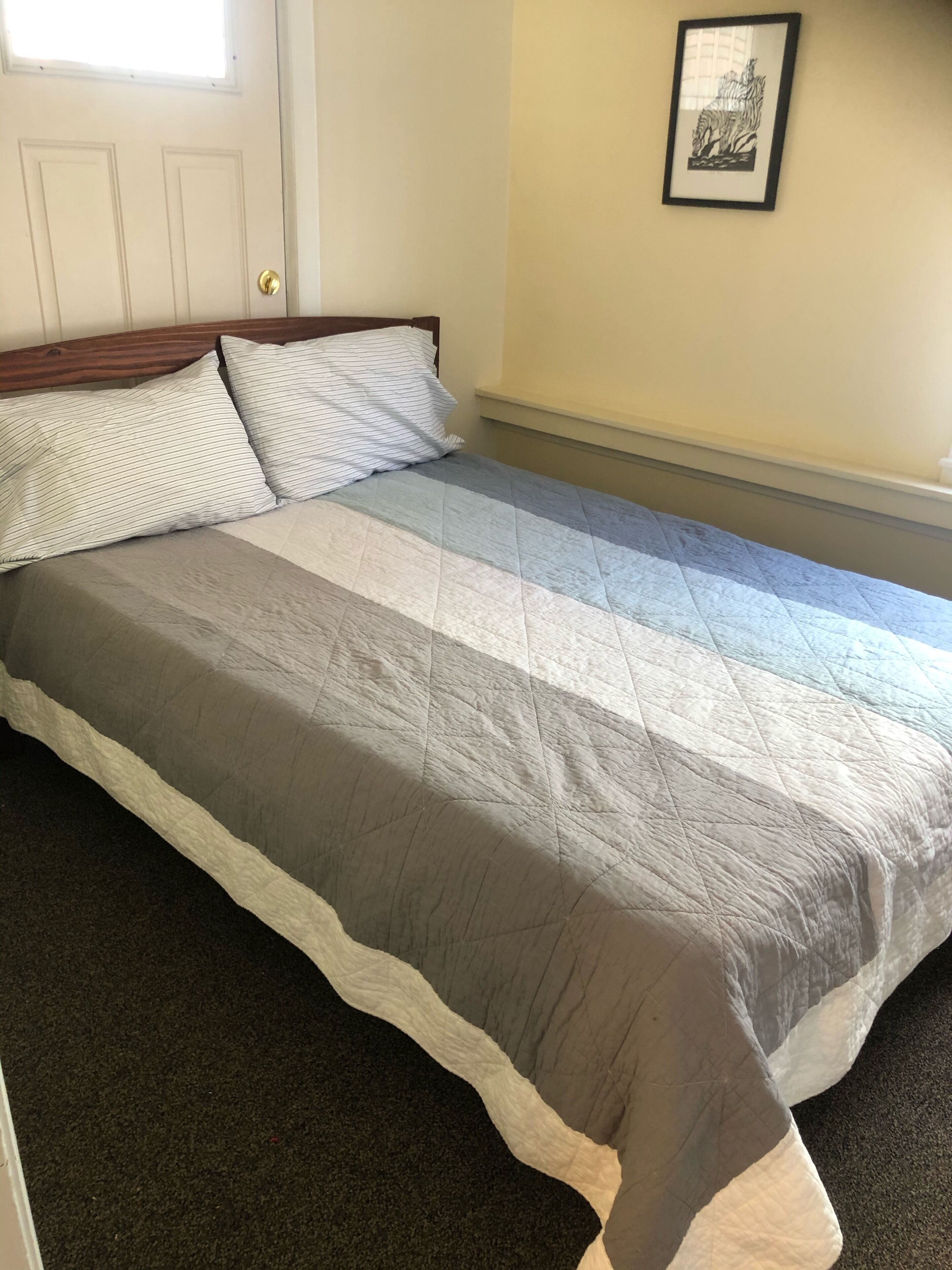 A bed with a quilted bedspread, a wooden headboard, and a framed picture on the wall.
