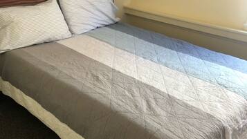 A bed with a quilted bedspread, a wooden headboard, and a framed picture on the wall.