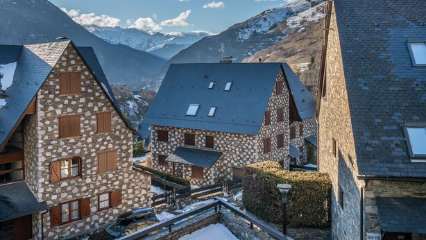 Een stenen gebouw met een hellend dak, een houten omheining en een met sneeuw bedekte berg op de achtergrond.