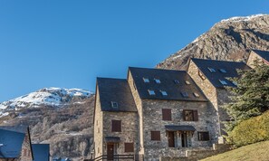 Un bâtiment en pierre doté de nombreuses fenêtres et d’une porte, se dressant sur un fond de paysage montagneux.