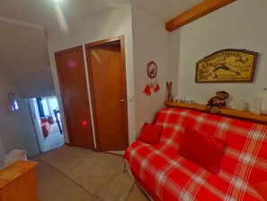 A room with a red plaid sofa, wooden doors, a wall-mounted sign, and a small shelf with decorative items. - Ski-in Studio, South, Parking, Pets Allowed (La Tania)