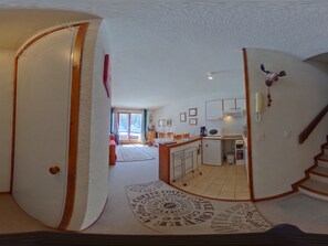 A compact kitchen with a microwave, a refrigerator, and a small sink. There is a dining area with a table and chairs, and a staircase leading to an upper level.