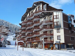 A multi-story hotel with balconies, a sign for 'Pain Bread Patisserie', and a ski resort in the background. - Ski-in Studio, South, Parking, Pets Allowed (La Tania)