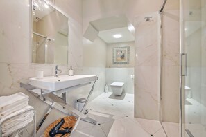 A modern bathroom with a glass shower enclosure, a white sink with a mirror above, and a toilet.