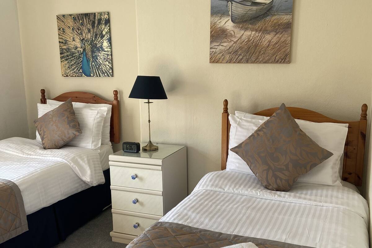 A hotel room with two beds, a nightstand with a lamp, and artwork on the walls.