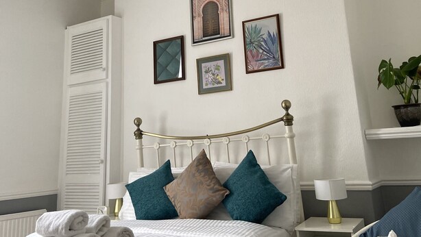 A neatly arranged bedroom with a bed, bedside tables, a nightstand, a lamp, and a potted plant.