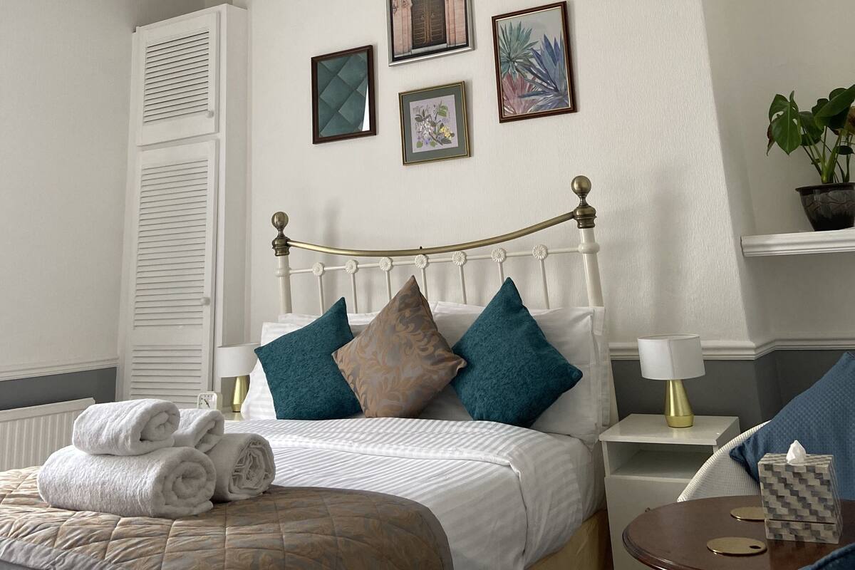 A neatly arranged bedroom with a bed, bedside tables, a nightstand, a lamp, and a potted plant.