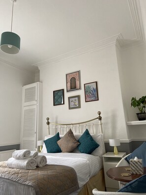 A neatly arranged bedroom with a bed, bedside tables, a nightstand, a lamp, and a potted plant. - The Mountview (Scarborough)