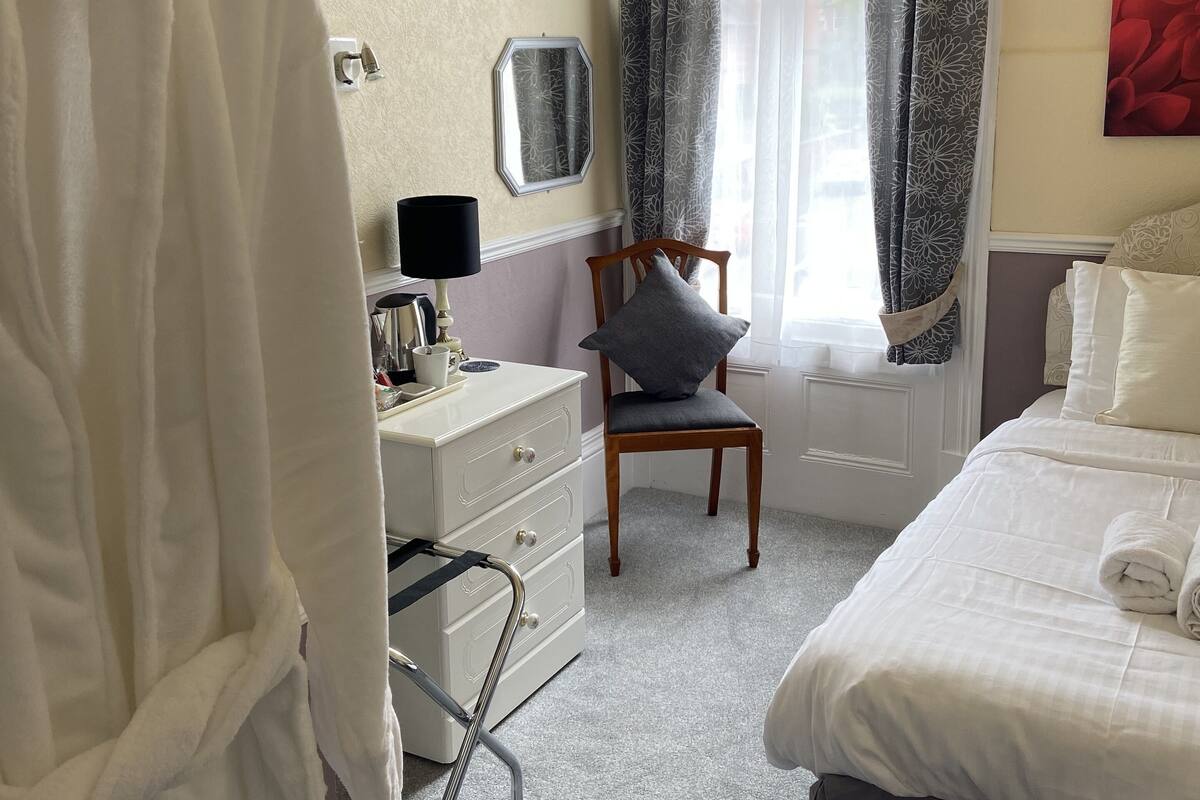 A hotel room with a bed, a chair, a dresser, and a window with curtains.