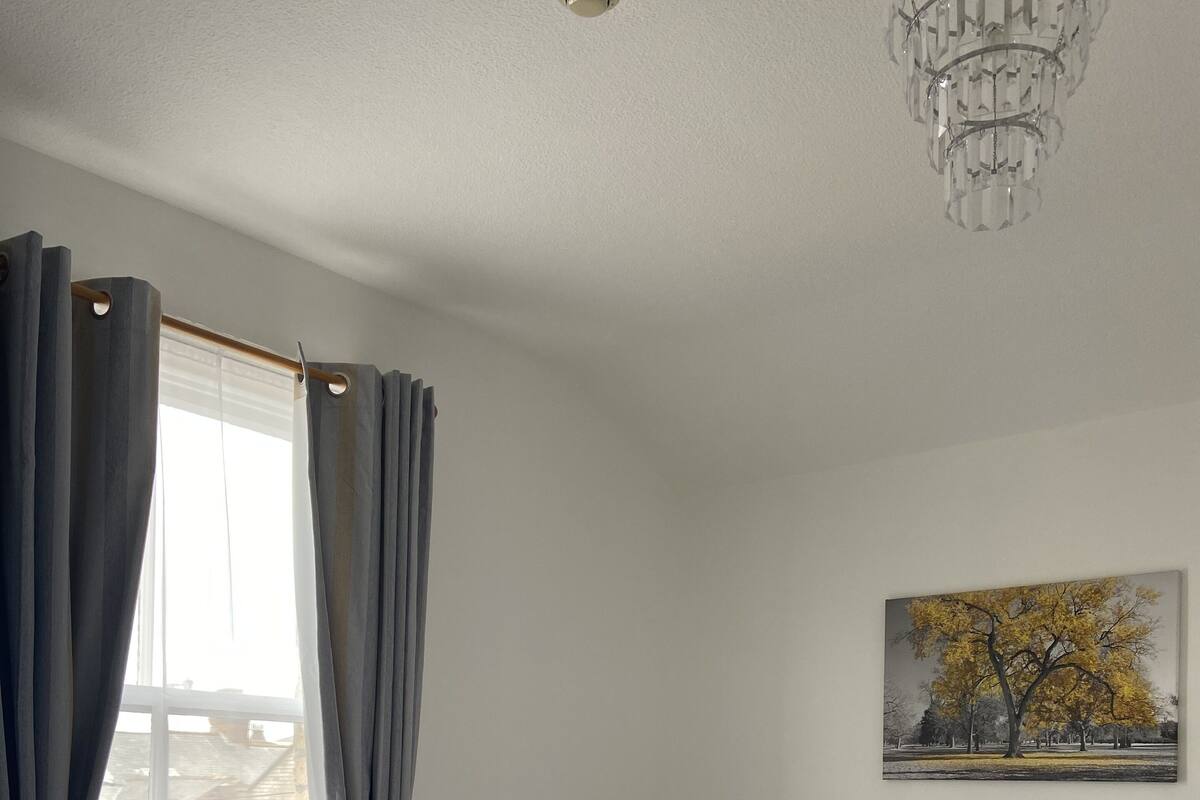 A neatly made bed with white and brown bedding, a bedside table with a lamp, and a painting of a tree on the wall.