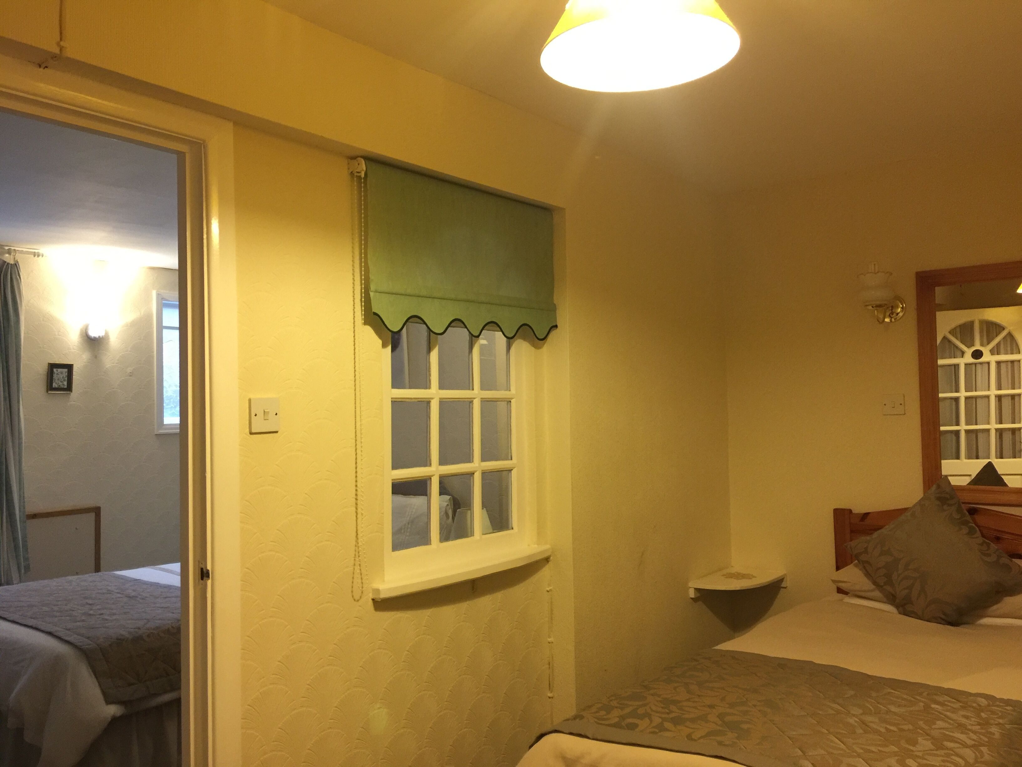 A bedroom with a bed, a window with a green valance, a bedside table, and a nightstand.