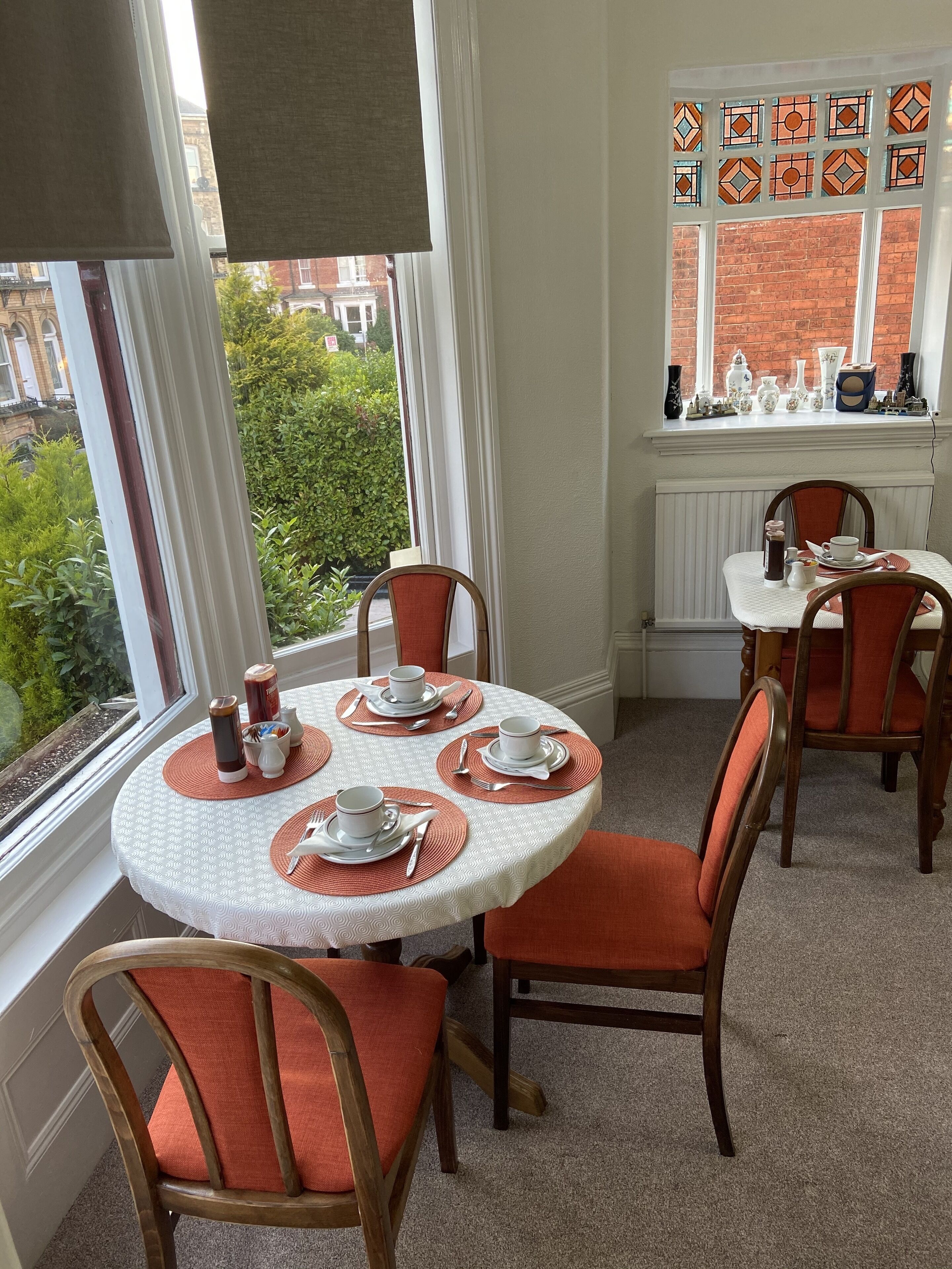 A dining area with a round table set for four, surrounded by wooden chairs with orange cushions.