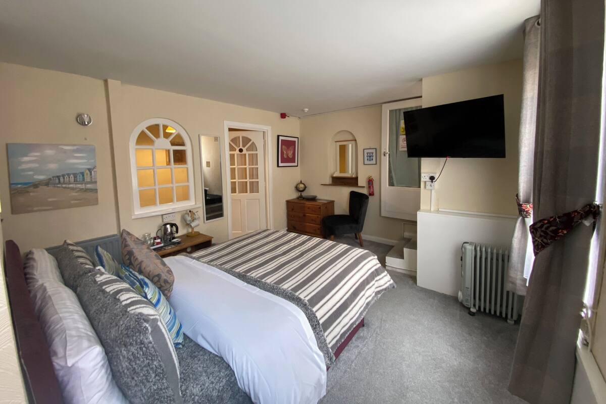 A hotel room with two beds, a desk, a chair, a TV, and a radiator.