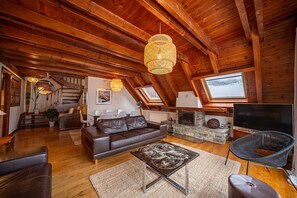 Een ruime loft met een houten plafond, een stenen openhaard, een leren bank en een grote televisie.
