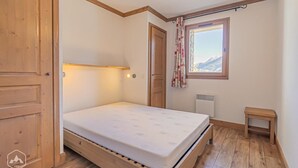 A small, single-bed room with wooden flooring, a window with a mountain view, a radiator, and a small bedside table. - 300m from ski slopes, floor -2, balcony, tv, 50m², Aussois (Aussois)