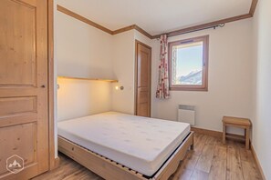 Una habitación pequeña con cama individual, suelo de madera, ventana con vista a la montaña, radiador y mesita de noche.