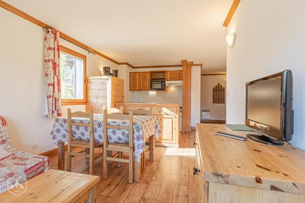 Una habitación acogedora de estilo cabaña con una mesa de comedor de madera, sillas, un televisor y una cocina con armarios de madera y un microondas.