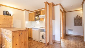 A compact kitchen with wooden cabinets, a built-in oven, a washing machine, and a coffee machine. - 300m from ski slopes, floor -2, balcony, tv, 50m², Aussois (Aussois)