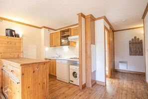Cocina compacta con armarios de madera, horno integrado, lavadora y cafetera.