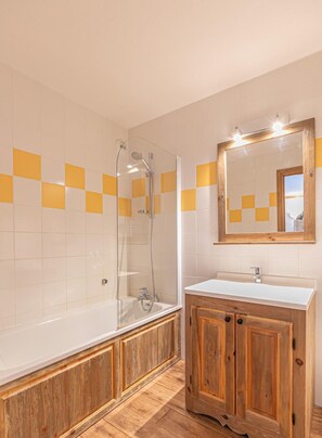 A bathroom with a bathtub, a wooden vanity, and a mirror with lights.