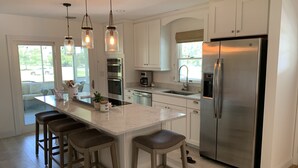 Une cuisine moderne avec des meubles blancs, des appareils en acier inoxydable et un îlot central doté de tabourets de bar.