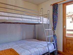 A bunk bed room with a ladder, a wooden door, and a colorful curtain.
