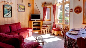 A cozy living room with a red sofa, a television, wooden walls, and a dining area with a table set for two.