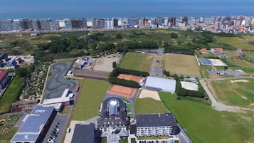 Vue aérienne d’une zone côtière comprenant un vaste complexe de bâtiments, notamment un terrain de sport, des aires de stationnement et une installation de panneaux solaires.