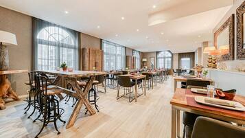 A spacious dining area with multiple tables and chairs, large windows, and a modern interior design.