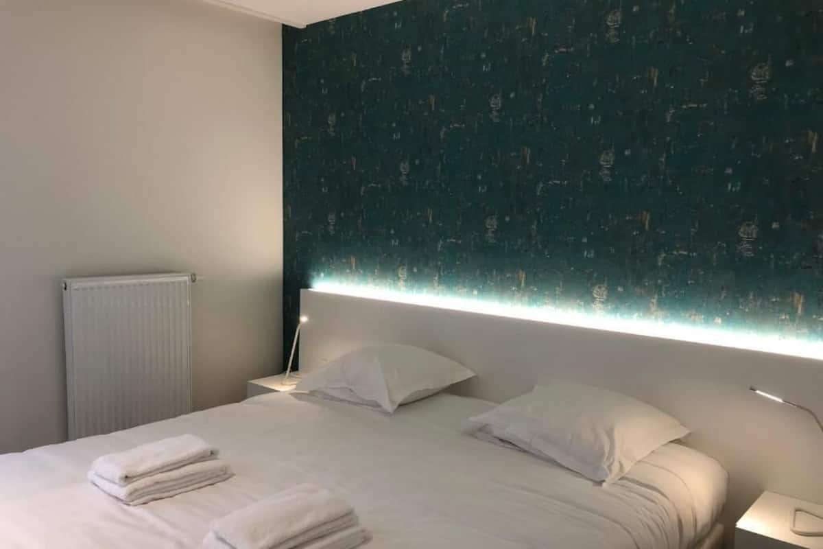 A hotel room with a large bed, two pillows, a bedside table with a lamp, and a wall with a textured pattern.