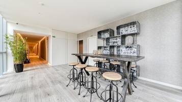 Een moderne bar met een lange tafel en krukken, een kamerplant en decoratieve objecten aan de muur.