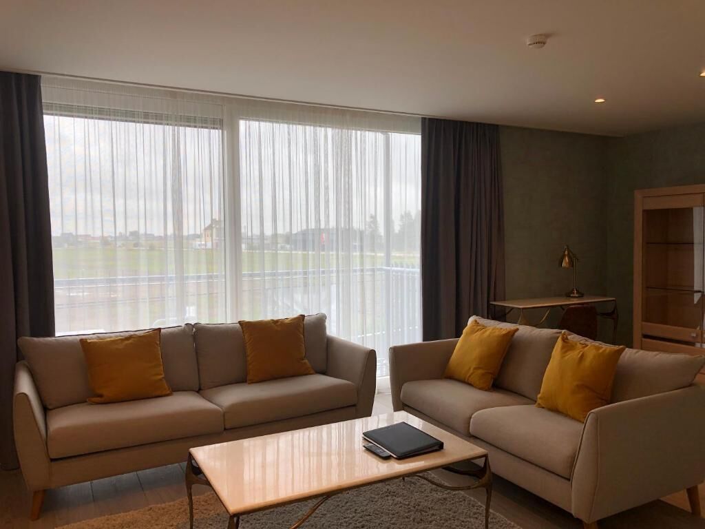 A modern living room with two sofas and a coffee table, large windows with curtains, a small side table, and a bookshelf.