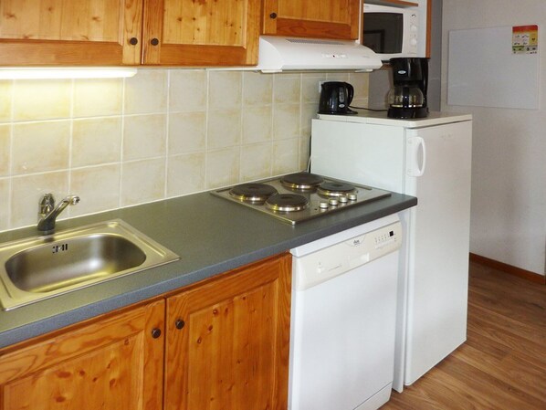 A compact kitchen with wooden cabinets, a stainless steel sink, a built-in microwave, a coffee maker, and a dishwasher. - Cozy 2-Room Apartment for 6 with Pool, Jacuzzi, Sauna, and Mountain Views (Les Orres)
