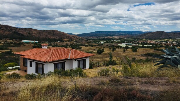 A house with a red-tiled roof, surrounded by dry grass and mountains in the background. - Hotel Duna Campestre (Sáchica)