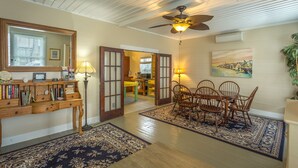 A dining area with a wooden table and chairs, a ceiling fan, and a painting on the wall. - Heart of Historic Apalachicola, Nostalgic Florida “Blue Moon Cottage ” (Apalachicola)