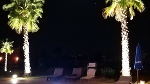 Ein Poolbereich bei Nacht mit beleuchteten Palmen und Liegestühlen.