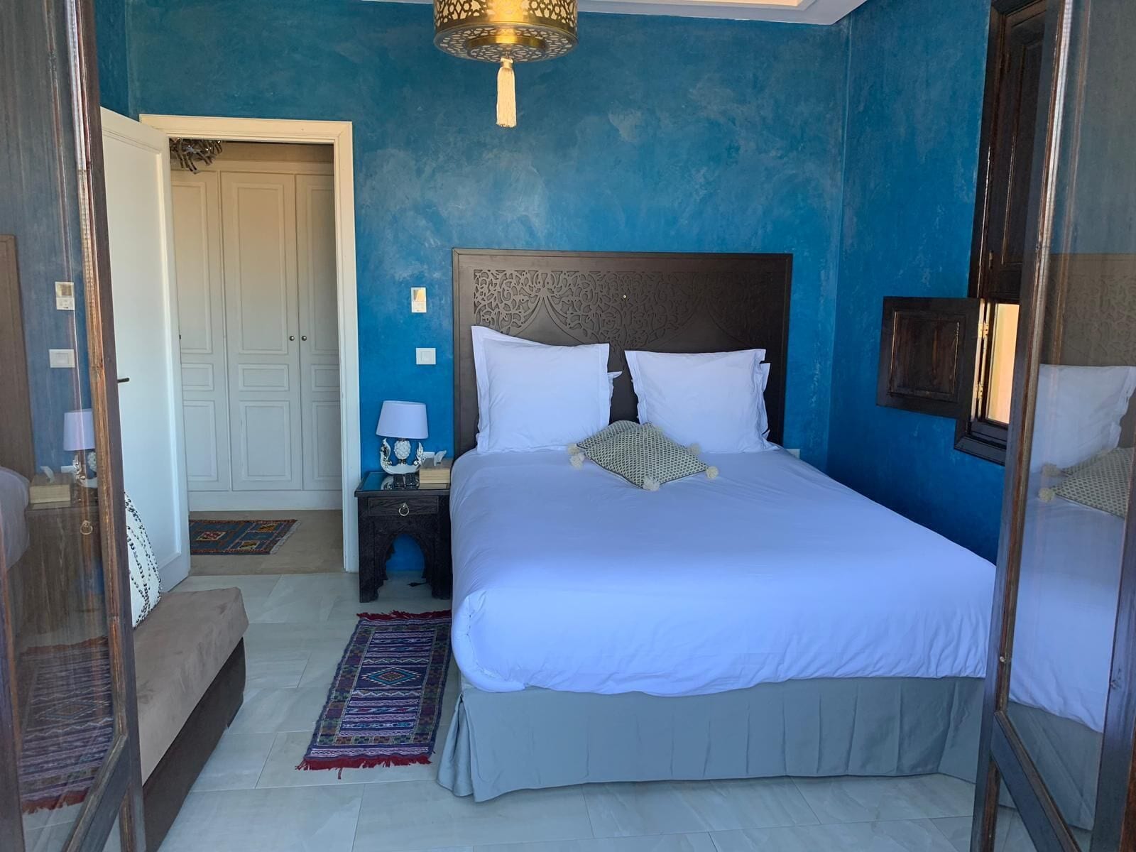 Quarto com cama grande, mesa de cabeceira, abajur e tapete estampado.