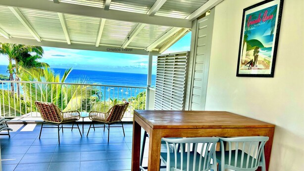 A balcony with a view of the ocean, a wooden table, and two chairs. - Studio Grande Anse Residence "O Coeur de Deshaies". Incredible seaview. (Deshaies)