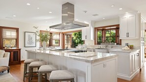 Uma cozinha espaçosa com uma ilha grande, armários brancos e uma coifa moderna de aço inoxidável.