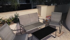 An outdoor seating area with two chairs and a table, surrounded by plants and a low wall.